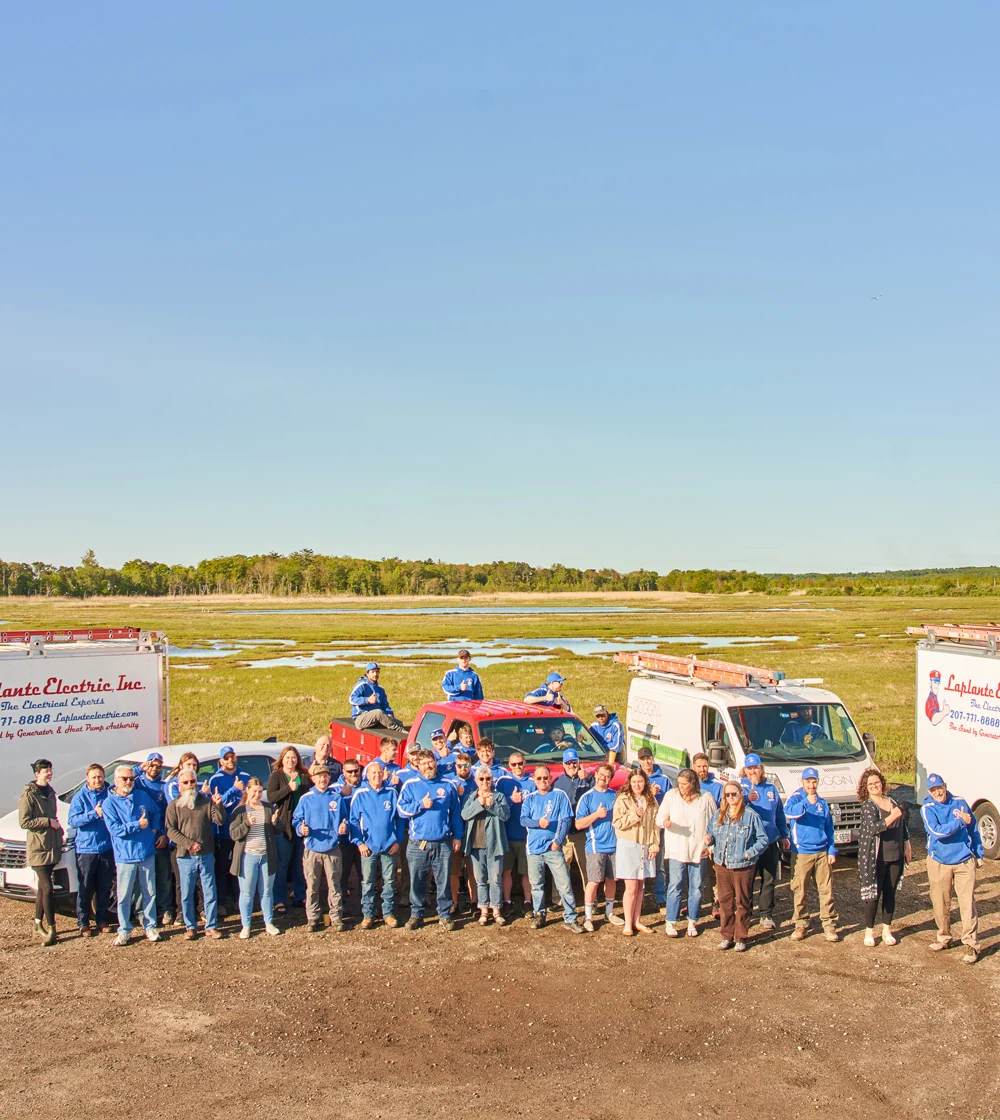 A group of LaPlante electricians stands in front of two white vans and a red 