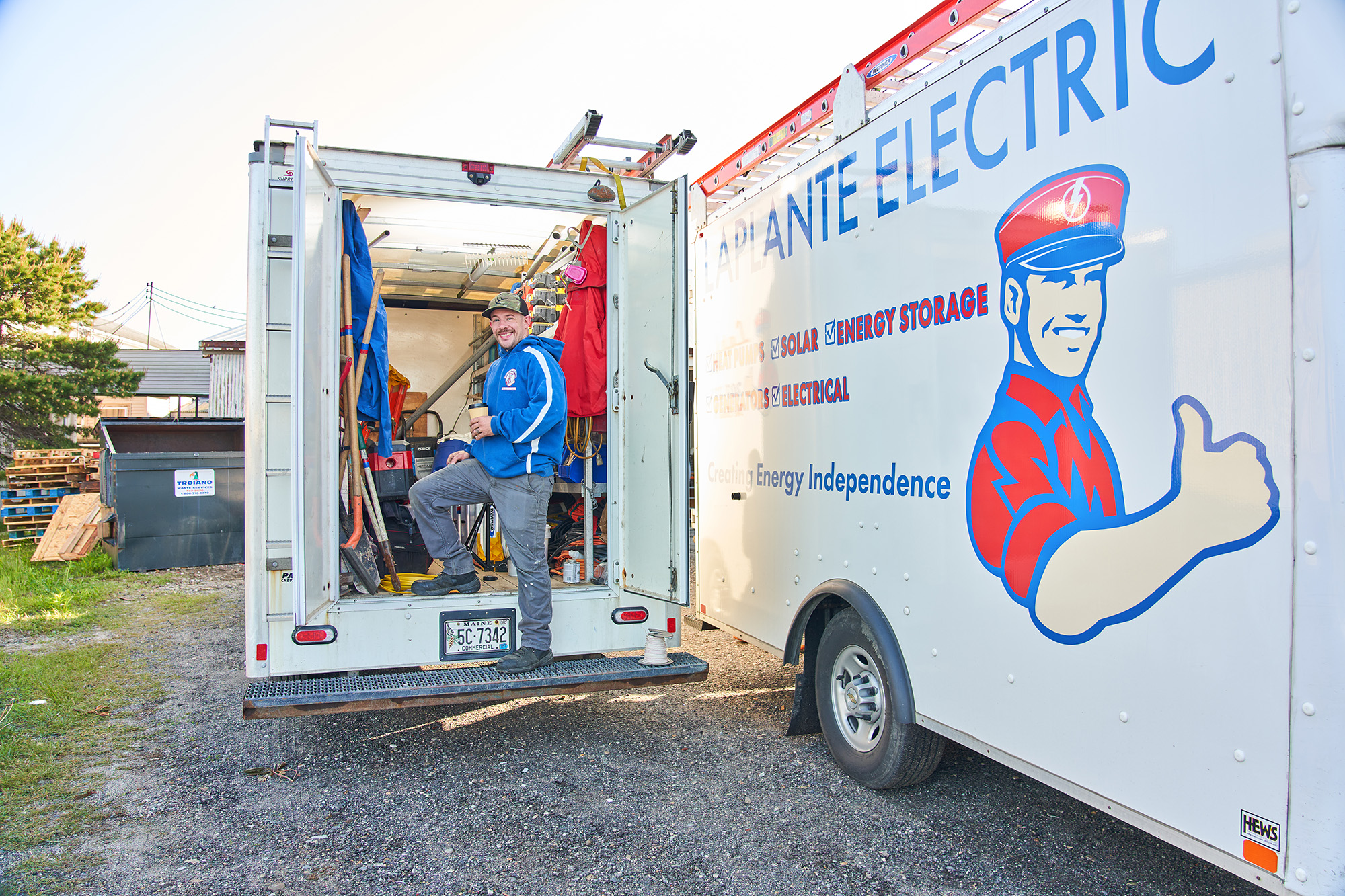 A person in a blue jacket stands at the back of an open utility truck, holding the door. 