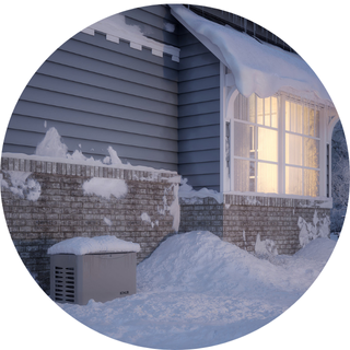 Snow piles up against a Scarborough, ME house with grey siding, brick foundation, lit window, heat pump, and nearby generator.